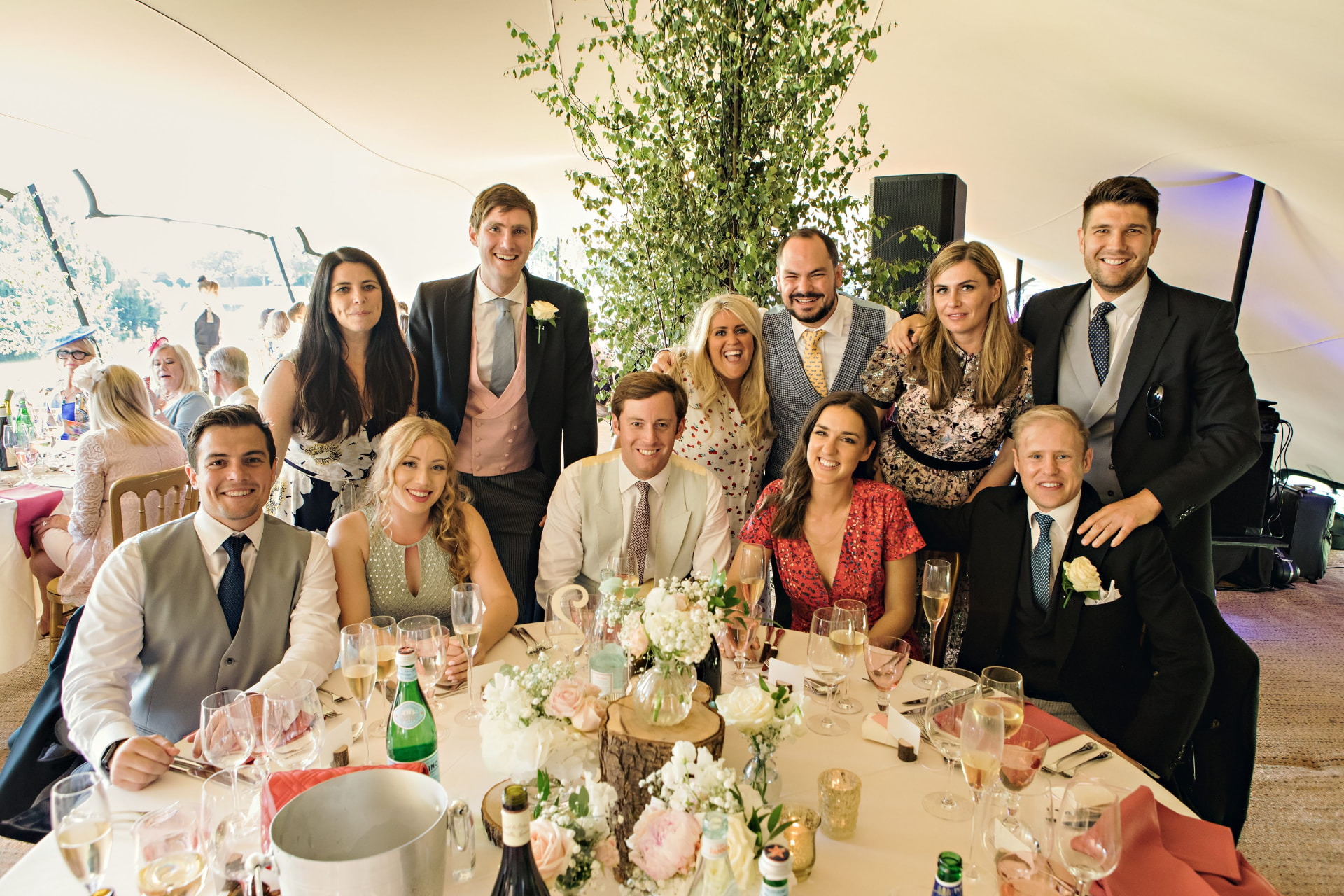 Wedding party gathered around a decorated round table in a marquee